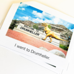 A picture of a photo book of a person going to Drumheller It is a photo of the welcome sign with a statue of a t rex